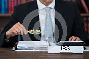 Auditor Examining Documents With Magnifying Glass At Table