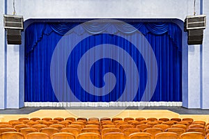 The auditorium in the theater. Blue curtain on the stage. Blue-brown chair. Room without people