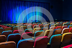 The auditorium in the theater. Blue-green curtain on the stage. Multicolored spectator chairs. Lighting equipment