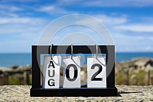 Aug 02 calendar date text on wooden frame with blurred background of ocean.