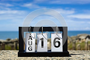 Aug 16 calendar date text on wooden frame with blurred background of ocean.