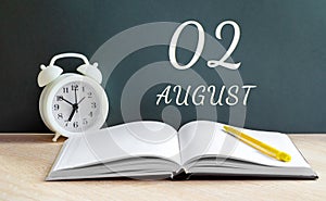 august 02. 02-th day of the month, calendar date.A white alarm clock, an open notebook with blank pages, and a yellow