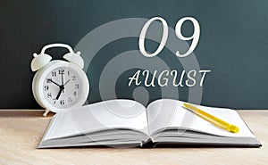 august 09. 09-th day of the month, calendar date.A white alarm clock, an open notebook with blank pages, and a yellow