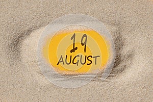 August 19. 19th day of the month, calendar date. Hole in sand. Yellow background is visible through hole