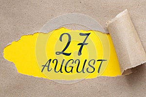 august 27. 27th day of the month, calendar date.Hole in paper with edges torn off. Yellow background is visible through