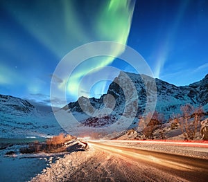 Aurora borealis on the Lofoten islands, Norway. Road traffic and blur car light. Green northern lights above mountains. Night sky