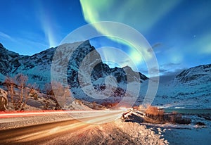Aurora borealis on the Lofoten islands, Norway. Road traffic and blur car light. Green northern lights above mountains. Night sky