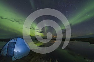 Aurora Borealis Northern lights above a camping tent in the Icelandic wilderness near lake