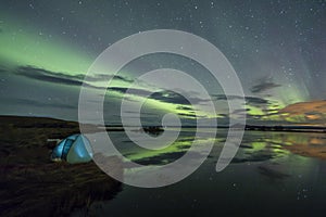 Aurora Borealis Northern lights above a camping tent in the Icelandic wilderness near lake