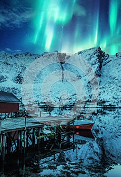 Aurora borealis, Northern lights over snow covered mountain and fishing village on arctic circle at Lofoten islands