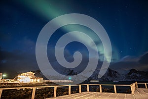 Aurora borealis or Northern lights over snowy mountain with house illumination at Mefjord Brygge