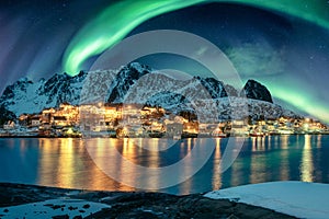 Aurora borealis over fishing village illumination on coastline in winter at Lofoten Islands