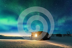 Aurora borealis over old small house with yellow light in window