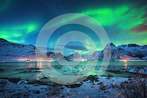 Aurora borealis over the sea coast, snowy mountains and city