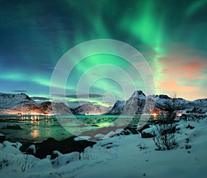 Aurora borealis over the sea coast, snowy mountains and city