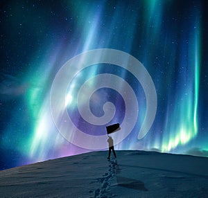 Aurora borealis over silhouette happy man standing waving flag on snowy mountain in arctic circle on winter