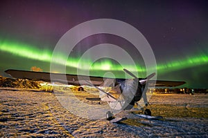 Aurora borealis over a small airplane on a frozen lake.