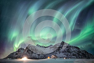 Aurora borealis with starry over snow mountain range with illumination house in Flakstad, Lofoten islands, Norway