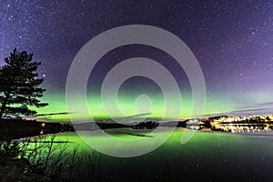 Aurora shines through the whole sky and stars reflecting at the lake, night Scandinavian countryside, autumn