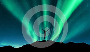 Aurora and silhouette of standing woman with raised up arms on the mountain in Norway. Aurora borealis