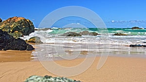 Australian coast with volcanic rocks at the shore, view from the beach to the horizon with blue water with waves on a summer