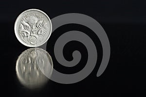 Australian coin five cents 1987 on the edge on black background with reflection