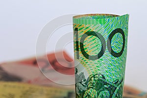 A rolled Australian hundred dollar note with a background of notes.