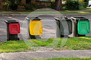 Australian garbage wheelie bins with colourful lids for recycling household waste and green garden waste lined up on the street