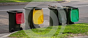 Australian garbage wheelie bins with colourful lids for recycling household waste and green garden waste lined up on the street