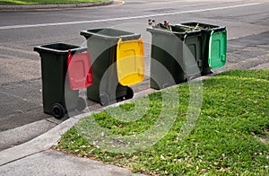 Australian garbage wheelie bins with colourful lids for recycling household waste and green garden waste lined up on the street