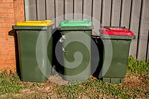 Australian garbage wheelie bins with red and yellow lids for general and recycling household waste and green lid for garden waste