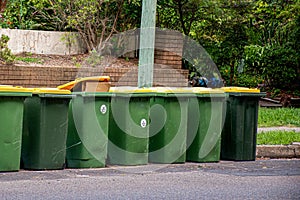 Australian garbage wheelie bins with yellow lids for recycling household waste lined up on the street kerbside for council rubbish