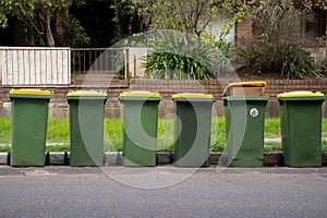 Australian garbage wheelie bins with yellow lids for recycling household waste lined up on the street kerbside for council rubbish