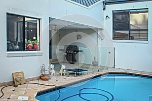 Australian house with pool with vaccum in it set in tile patio-outside room with glass safety fence keeping dogs out