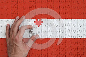 Austria flag is depicted on a puzzle, which the man`s hand completes to fold