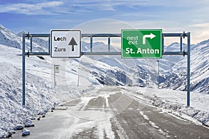 Austria green road sign ski town Lech, Zurs and St. Anton with a lot of snow and mountain sky background