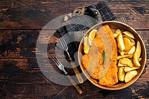 Austrian fried weiner schnitzel with potato wedges in a wooden plate. Wooden background. Top view. Copy space