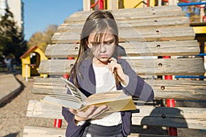 Autdoor portrait of offended little girl. Child reading book, offendedly pouting her lips
