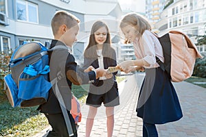 Outdoor portrait of smiling schoolchildren in elementary school. A group of kids with backpacks are having fun, talking. Education