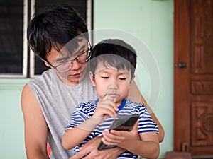 Authentic asian child boy and father watching to mobile phone together