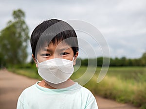 Authentic asian child boy wearing medical face mask to prevent from corona virus or covid-19 outdoor in nature background.
