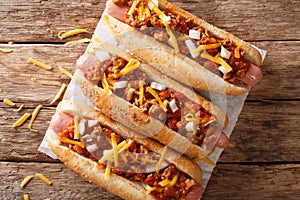 Authentic chili hot dog with cheddar cheese, onion and spicy sauce close-up on paper. Horizontal top view photo