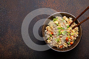 Authentic Chinese and Asian fried rice with egg and vegetables in ceramic brown bowl top view on dark rustic concrete