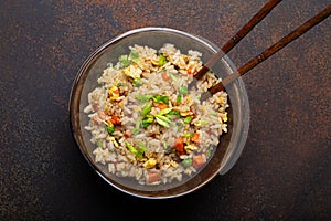 Authentic Chinese and Asian fried rice with egg and vegetables in ceramic brown bowl top view, dark rustic concrete