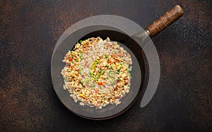 Authentic Chinese and Asian fried rice with egg and vegetables in wok top view, rustic concrete table background