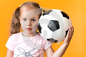 Authentic cute smiling preschool little girl with classic black and white soccer ball look at camera on yellow