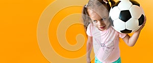 Authentic cute smiling preschool little girl with classic black and white soccer ball look at camera on yellow