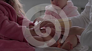 Authentic cute young woman applying face mask of baby girl. mom with 2 children daughters different ages in bathrobes