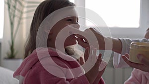 Authentic cute young woman applying face mask of baby girl. mom with 2 children daughters different ages in bathrobes