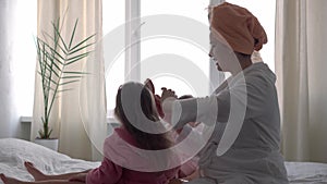 Authentic cute young woman combing long hair of baby girl. mom with 2 children daughters different ages in bathrobes